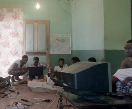 osm ghanských mužů sedí v prázdném pokoji a hledí do monitorů
