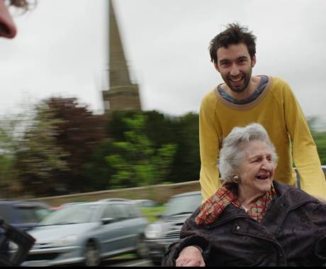 muž veze starou ženu na vozíku, oba se smějí