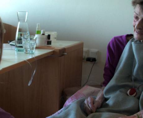 žena sedící u lůžka usmívající se pacientky