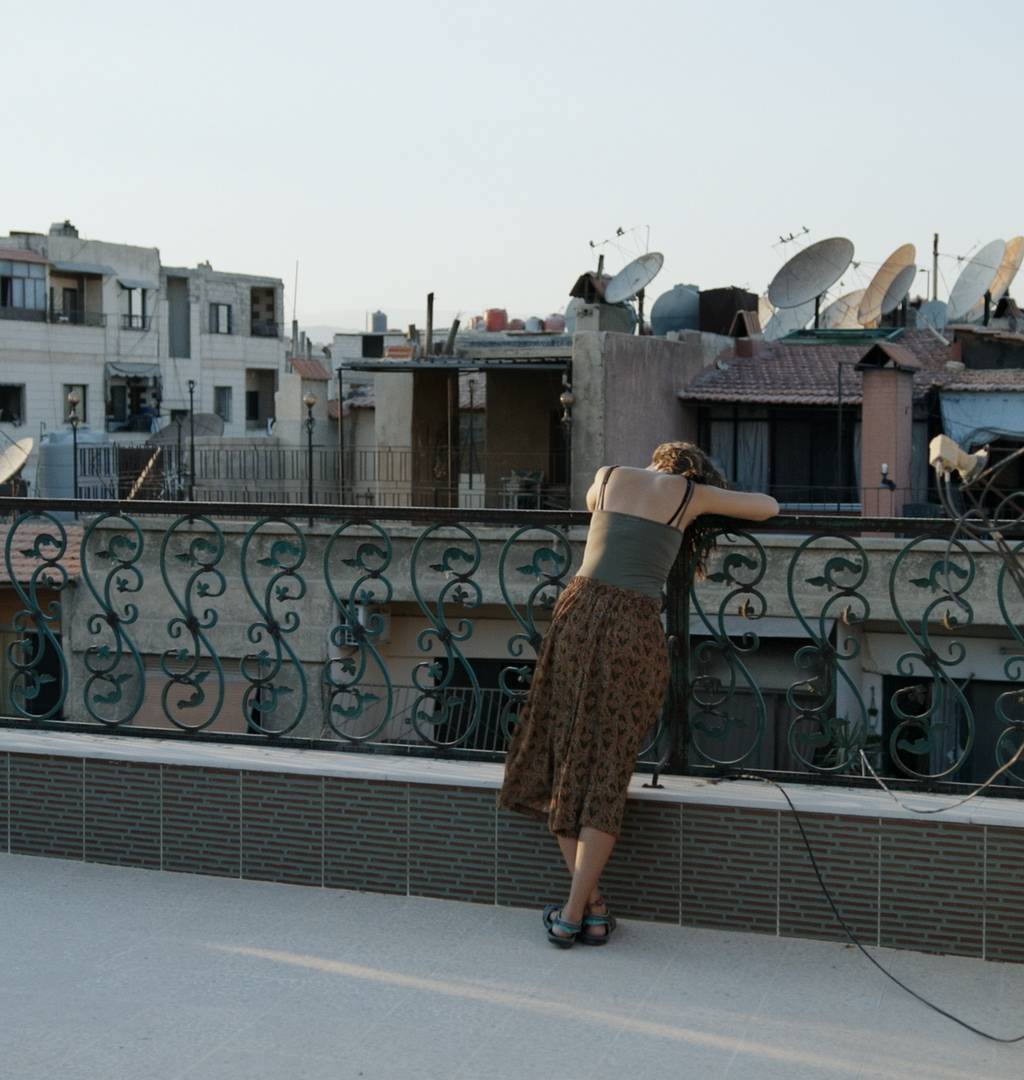 žena opírající se o zábradlí na terase, v pozadí domy