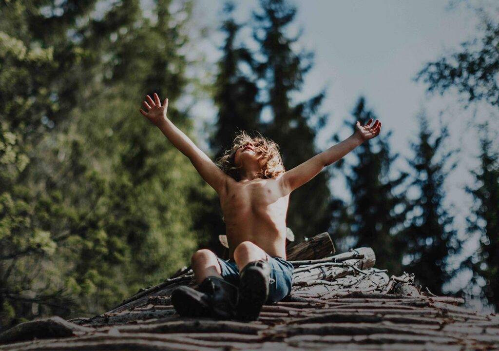 chlapec sedí na kládě stromu s rukama k obloze ve větru